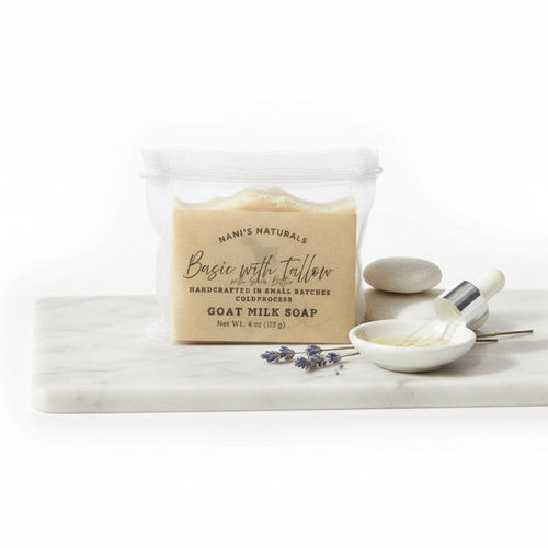 A  nylon pouch of Nan's Naturals Basic with Tallow goat milk soap  on a white marble board, with a small dish of white soap, a dropper, and lavender sprigs against a white background.